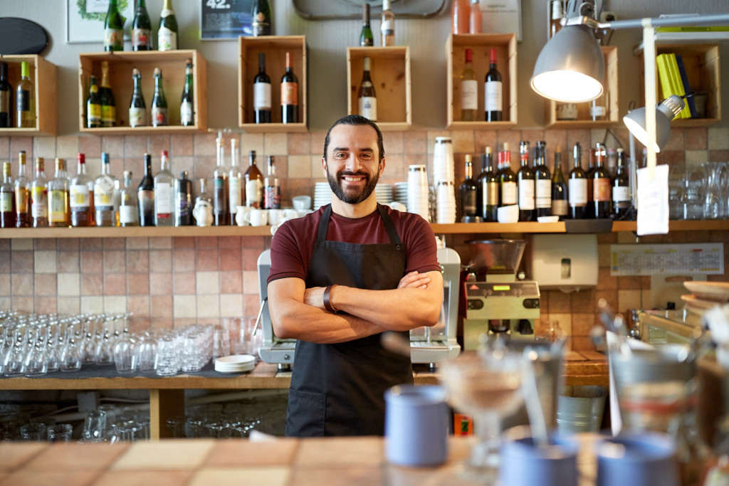 smiling waiter with apron behind bar or coffee shop