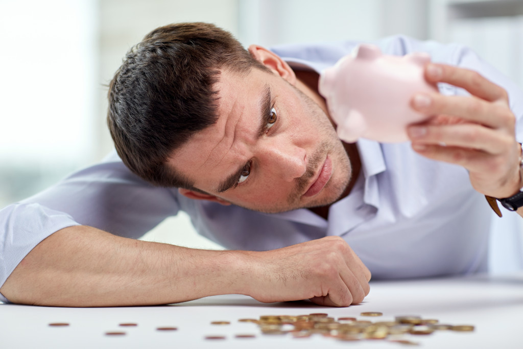 A person looking closely at an empty piggy bank with coins scattered on the table in front of him