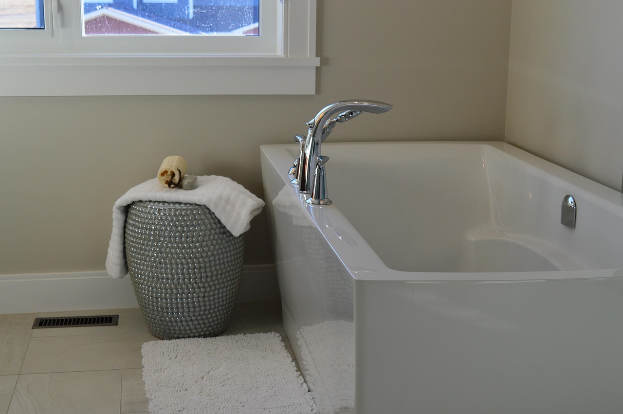 white ceramic bathtub and a two-handle faucet, with a white rug and a gray stool next to the tub