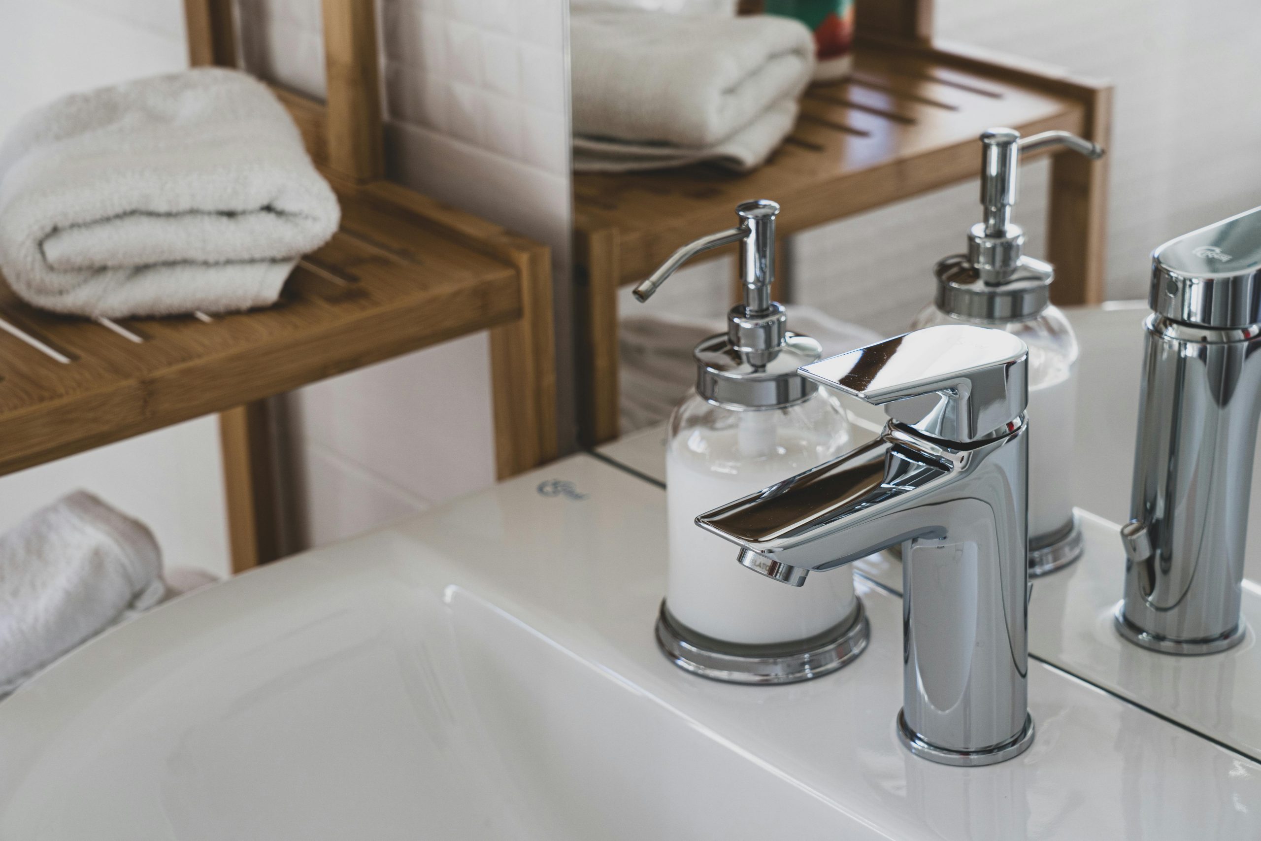 bathroom faucet on a ceramic sink, next to a shelf with folded towels